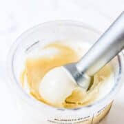 A scoop of Ninja Creami vanilla ice cream with vanilla bean specks being lifted from a Creami pint.