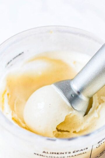 A scoop of Ninja Creami vanilla ice cream with vanilla bean specks being lifted from a Creami pint.