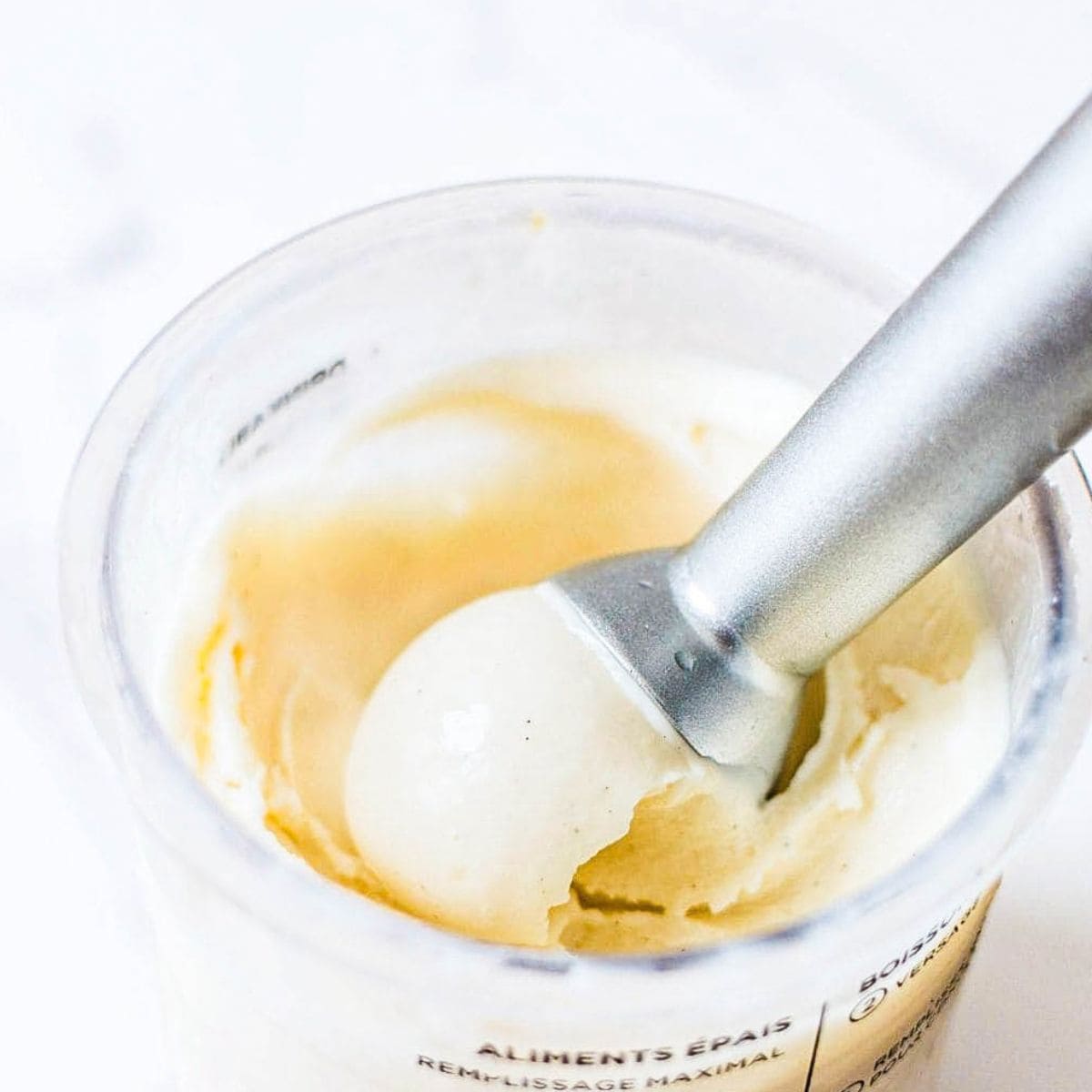 A scoop of Ninja Creami vanilla ice cream with vanilla bean specks being lifted from a Creami pint.