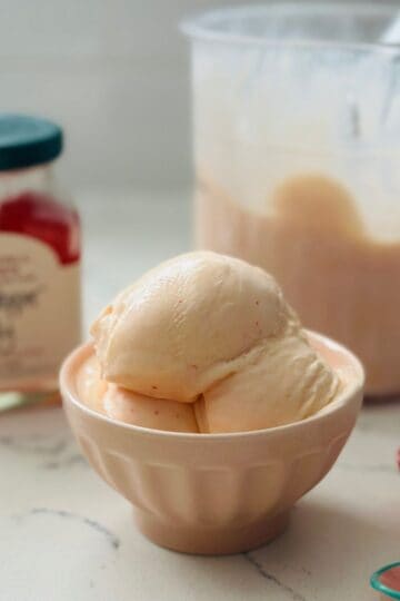 Small bowl with scoops of homemade red pepper jelly ice cream made in the Ninja Creami, showing creamy smooth texture and light peach color.