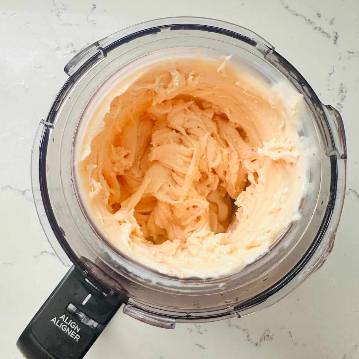 Spinning frozen red pepper jelly mixture in Ninja Creami machine to create smooth, creamy texture.