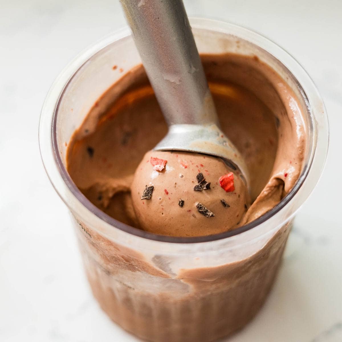 Chocolate strawberry ice cream swirled together in a dish with a spoon ready to scoop.