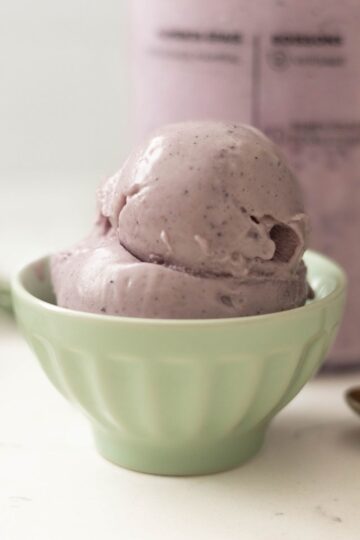 Two scoops of mixed berry Ninja Creami ice cream served in a small light green bowl with the pint blurred in the background.