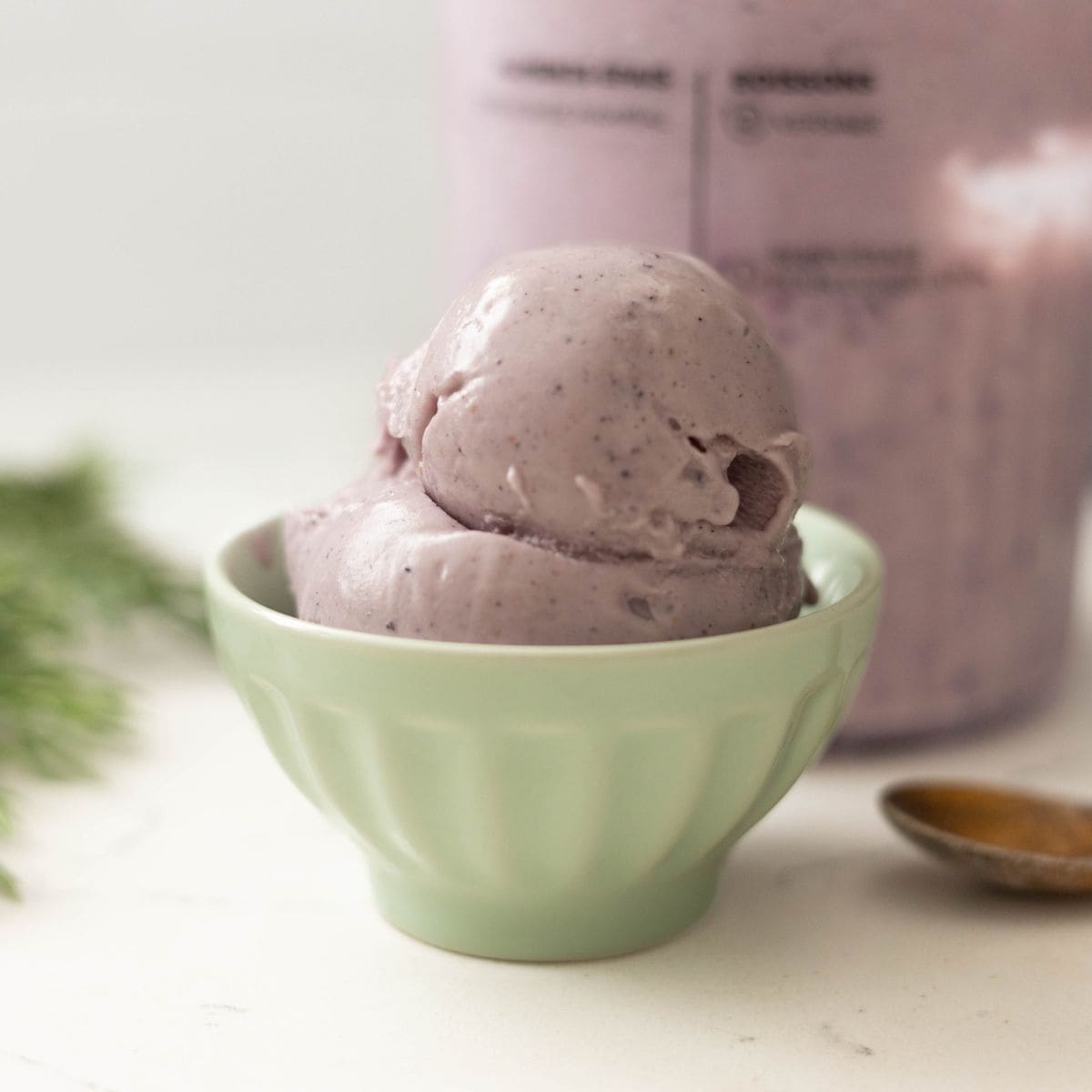 Two scoops of mixed berry Ninja Creami ice cream served in a small light green bowl with the pint blurred in the background.