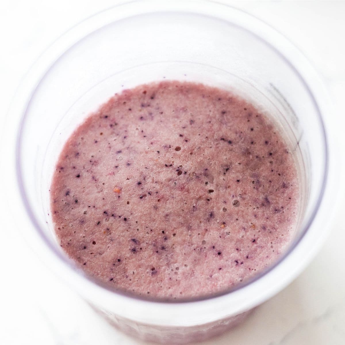 Top view of frozen Ninja Creami mixed berry base in the Deluxe pint, lightly pink with berry specks throughout.