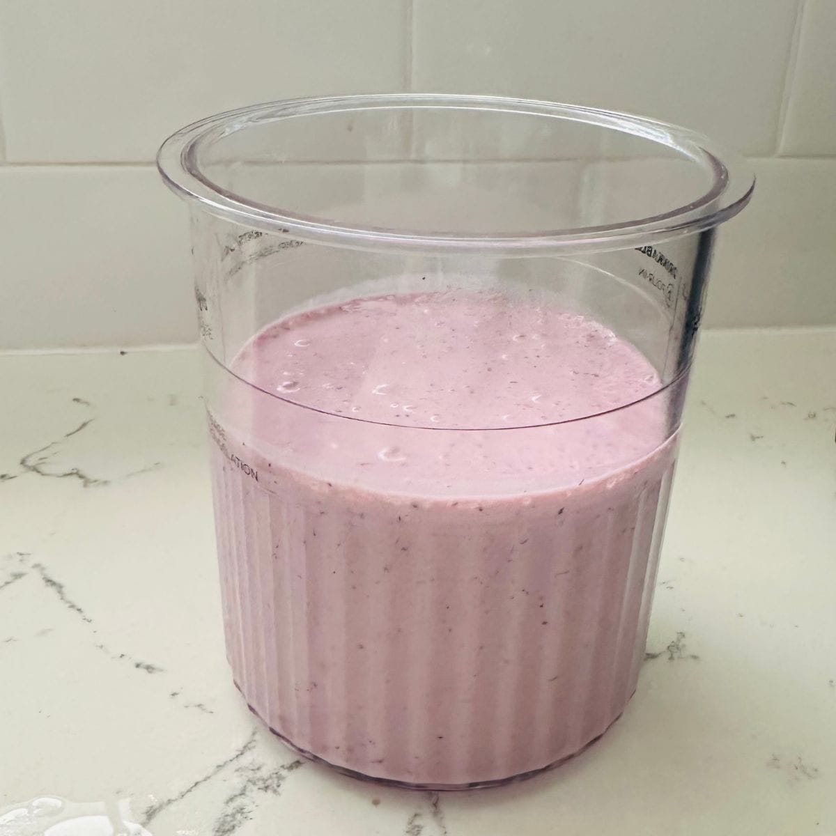 Blended mixed berry Ninja Creami base in the Deluxe pint before freezing, pale pink and filled near the freeze line.