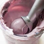 Close-up of creamy mixed berry Ninja Creami ice cream being scooped from the pint with a metal scoop.