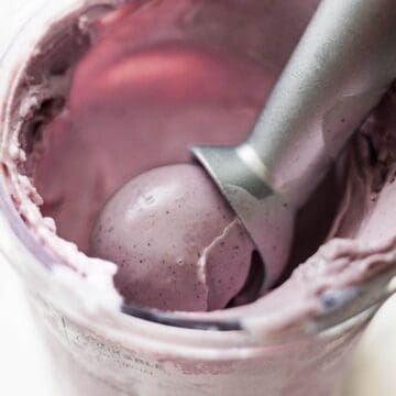 Close-up of creamy mixed berry Ninja Creami ice cream being scooped from the pint with a metal scoop.