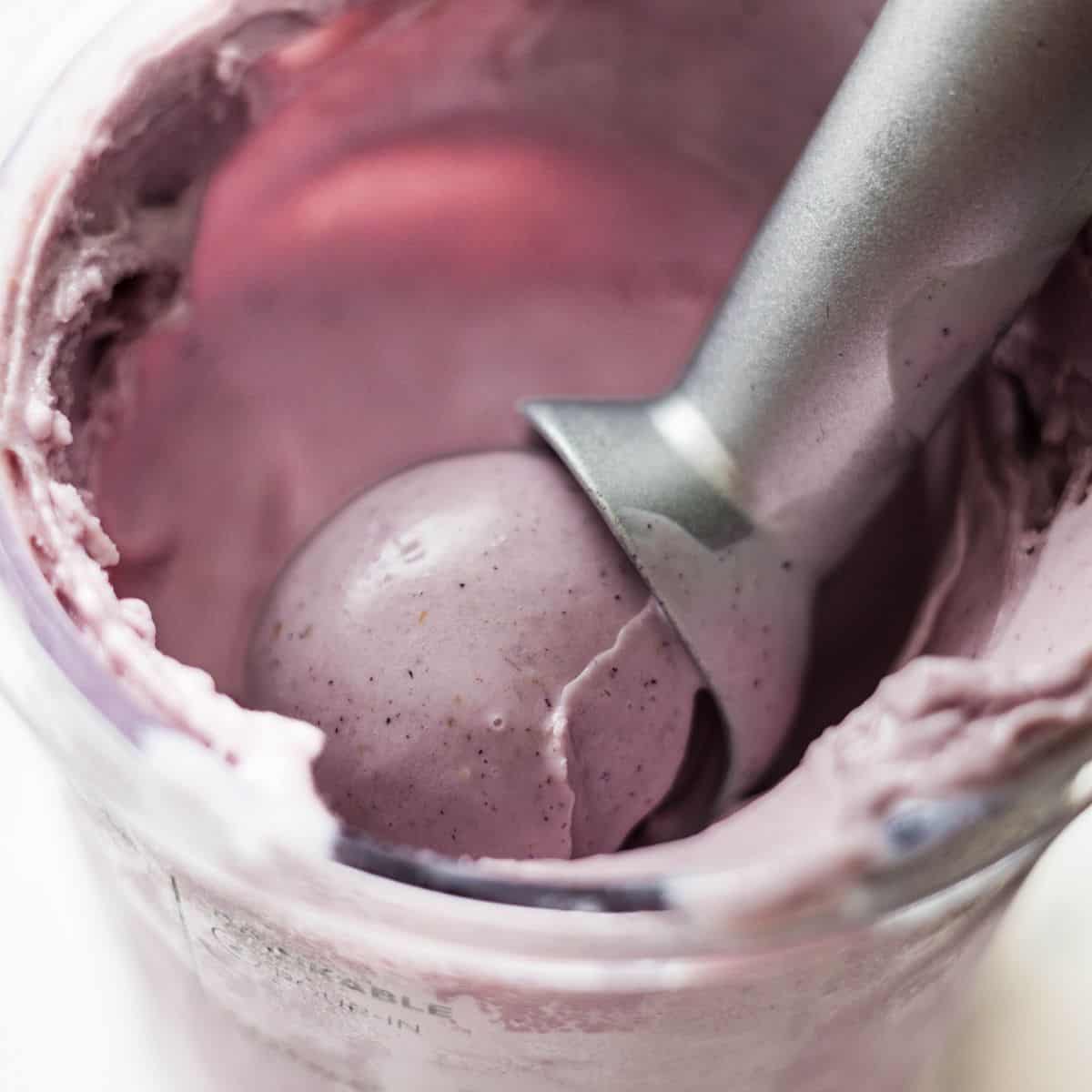 Close-up of creamy mixed berry Ninja Creami ice cream being scooped from the pint with a metal scoop.