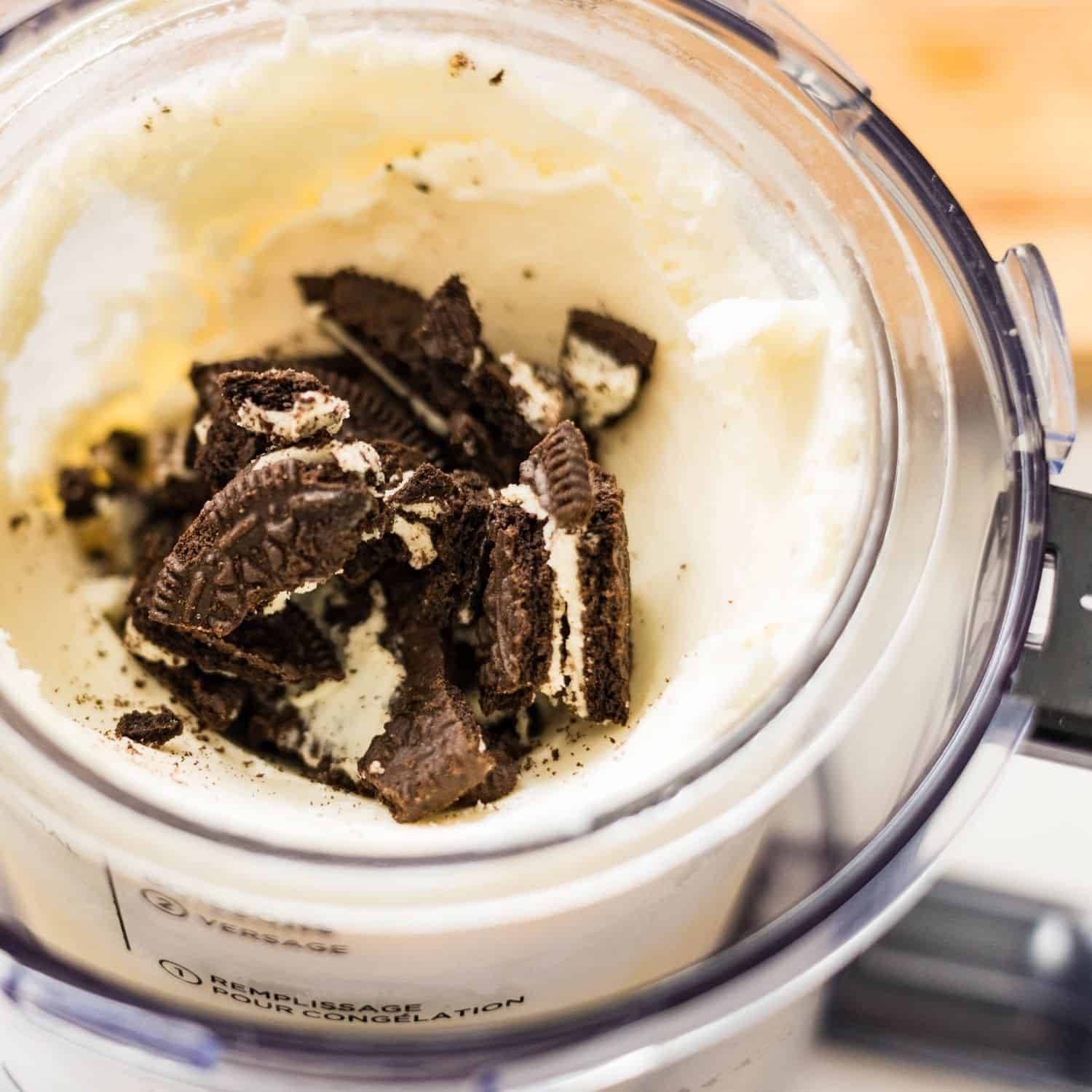 Broken chocolate sandwich cookies on a wooden cutting board, ready to use as mix-ins for high protein cookies and cream ice cream.