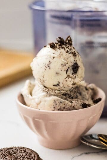 Scoops of high protein cookies and cream ice cream served in a small pink bowl with cookie crumbs on top.