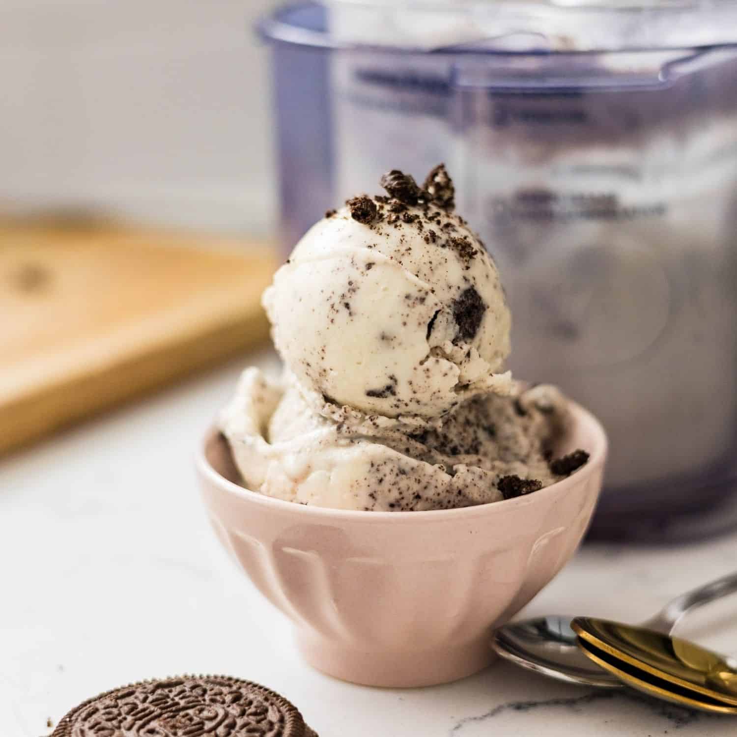 Scoops of high protein cookies and cream ice cream served in a small pink bowl with cookie crumbs on top.