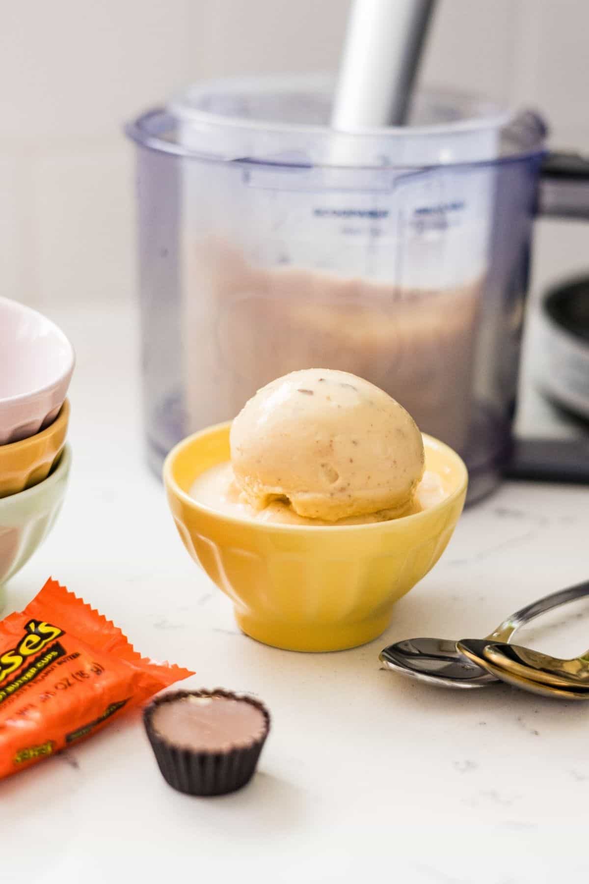 Scoops of Ninja Creami high protein peanut butter cup ice cream served in a yellow bowl with Reese’s peanut butter cups nearby