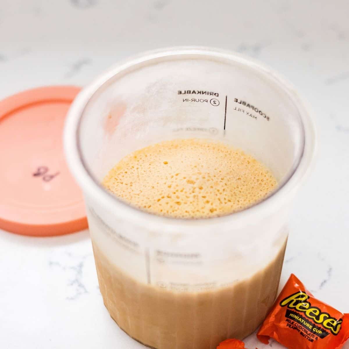 Peanut butter cup ice cream base in Ninja Creami pint container before freezing with Reese’s peanut butter cups on the side