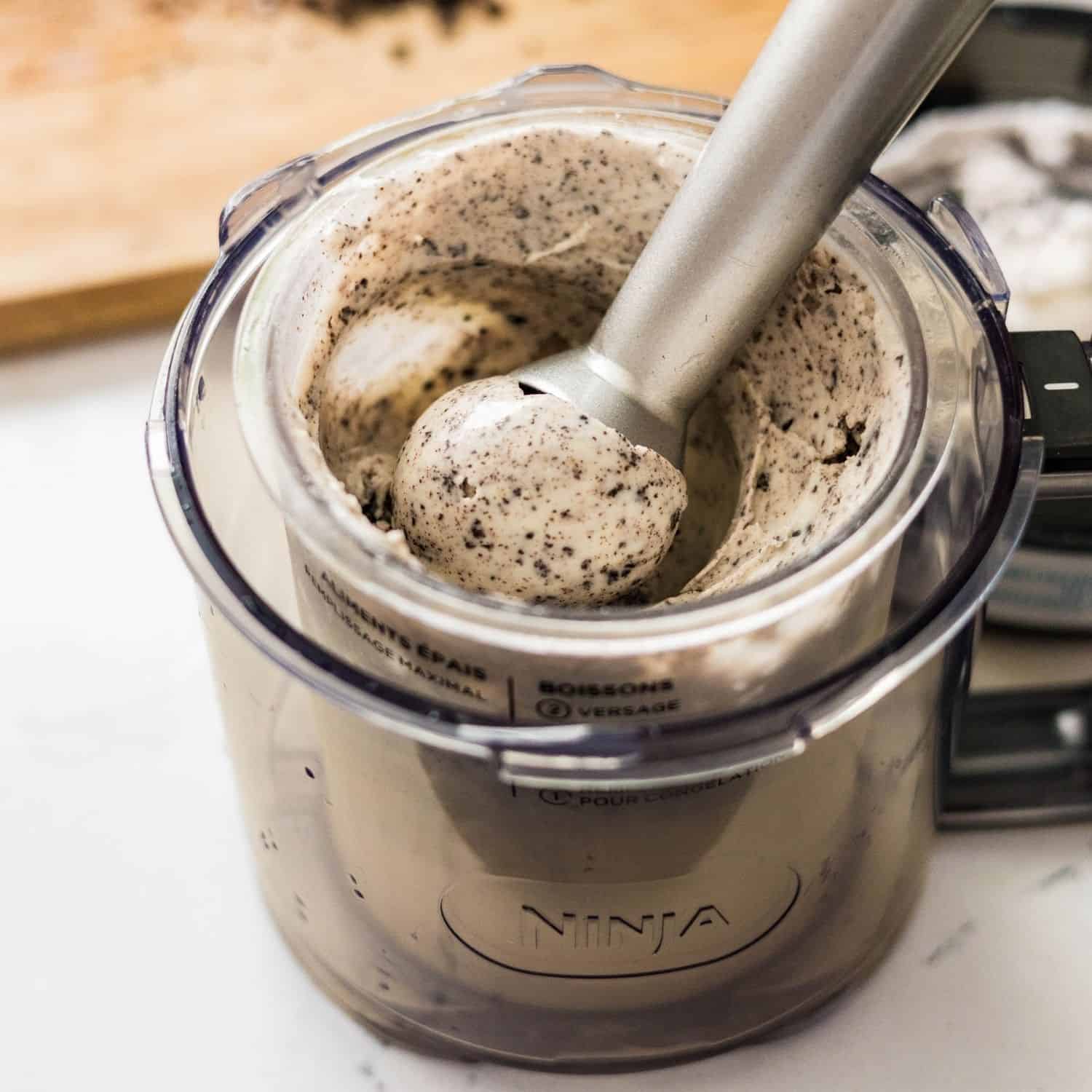 A scoop of creamy high protein cookies and cream ice cream lifted from a Ninja Creami pint, showing a smooth texture with cookie specks.