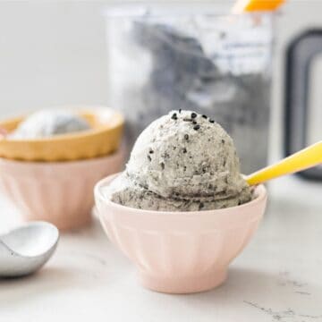 Homemade black sesame ice cream made in the Ninja Creami served in a bowl with the pint behind it