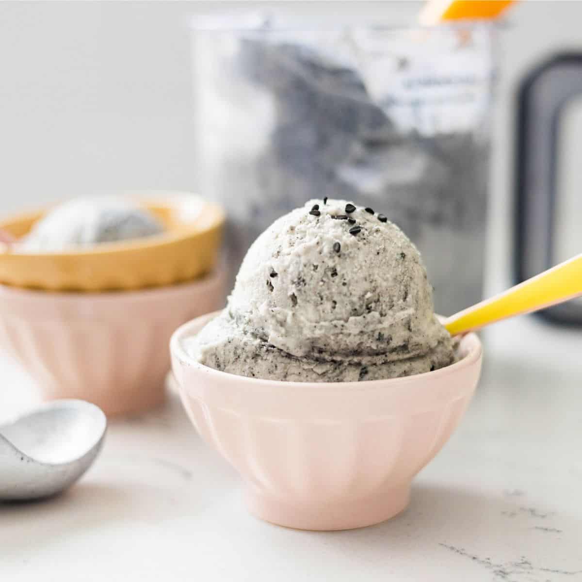 Homemade black sesame ice cream made in the Ninja Creami served in a bowl with the pint behind it
