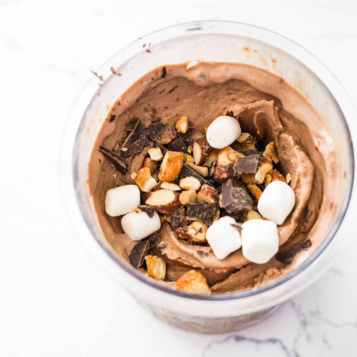 Chocolate ice cream in a Ninja Creami pint topped with rocky road mix-ins before mixing