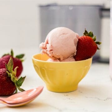 Ninja Creami strawberry protein frozen yogurt served in a yellow bowl with fresh strawberries