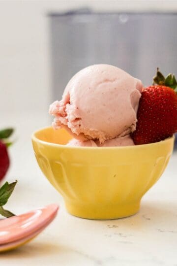 Ninja Creami strawberry protein frozen yogurt served in a yellow bowl with fresh strawberries