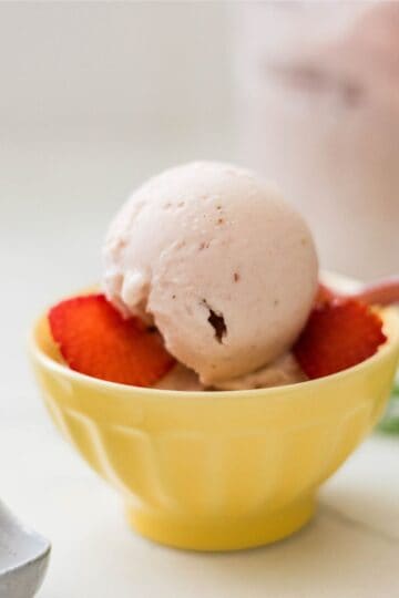 Ninja Creami strawberry banana ice cream served in a yellow bowl with sliced strawberries