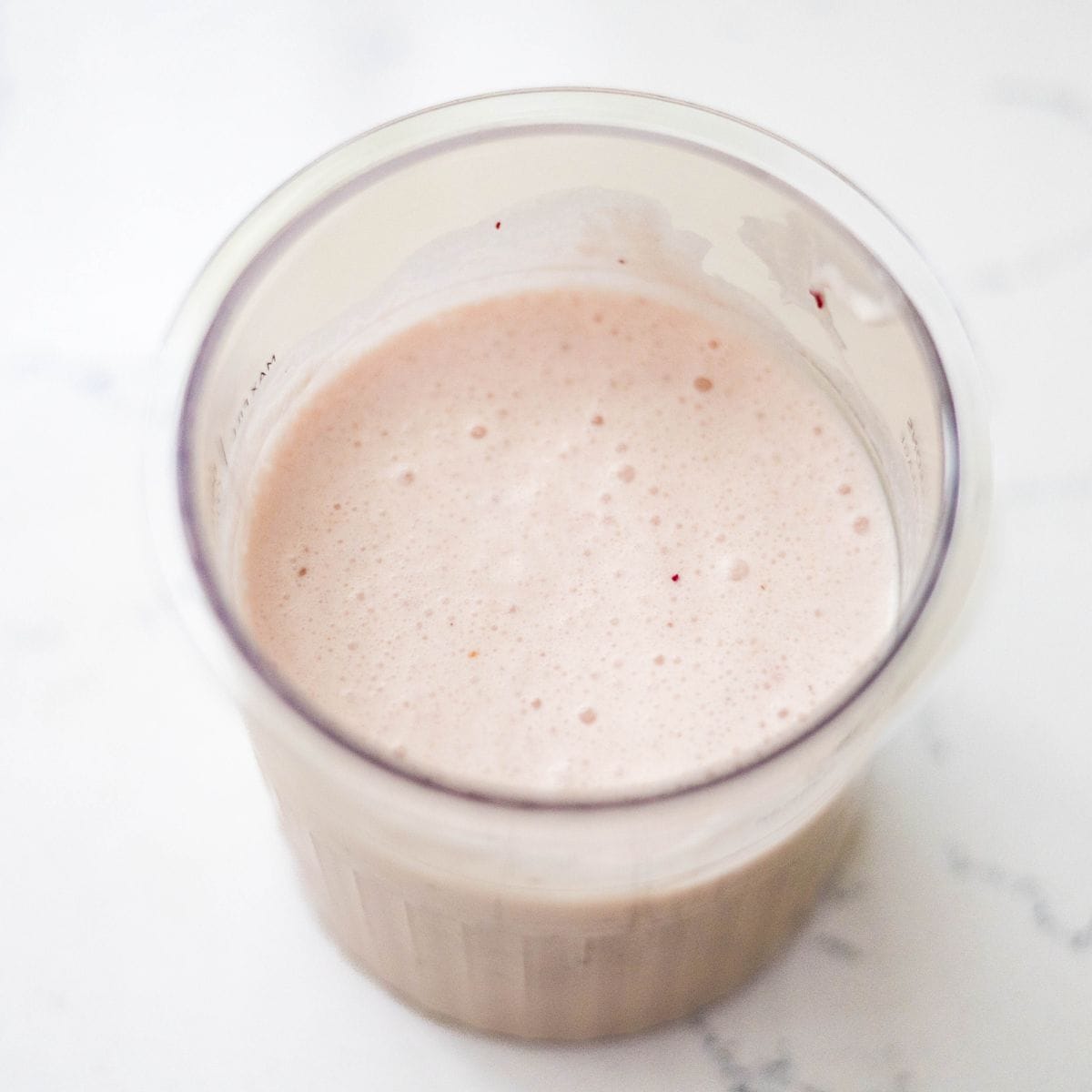 Blended strawberry banana ice cream mixture in a Ninja Creami pint before freezing