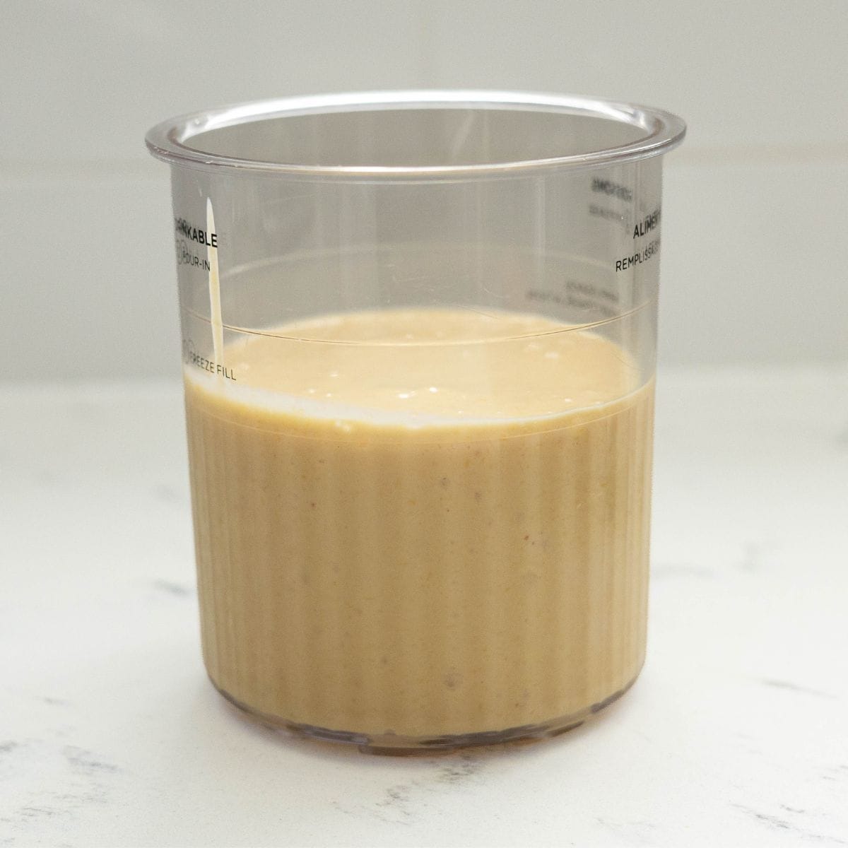 Blended mango Greek yogurt base in a Ninja Creami pint before freezing
