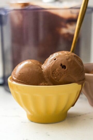 Two scoops of Ninja Creami chocolate peanut butter ice cream in a yellow bowl with a gold spoon