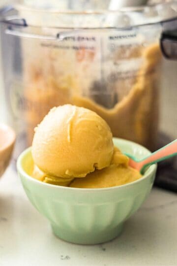 Scoops of Ninja Creami mango frozen yogurt in a mint green bowl with the Ninja Creami machine behind it