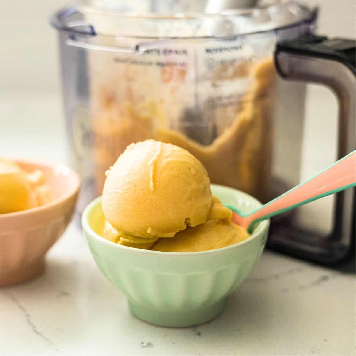 Scoops of Ninja Creami mango frozen yogurt in a mint green bowl with the Ninja Creami machine behind it