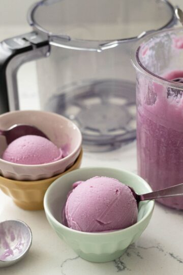 Scoops of Ninja Creami purple sweet potato protein ice cream in pastel bowls with spoons and the Ninja Creami machine behind them