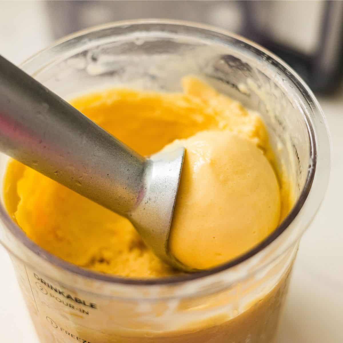 Ice cream scoop lifting mango frozen yogurt from a Ninja Creami pint