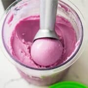 Bowl of mashed purple sweet potato with a fork, next to a whole purple sweet potato